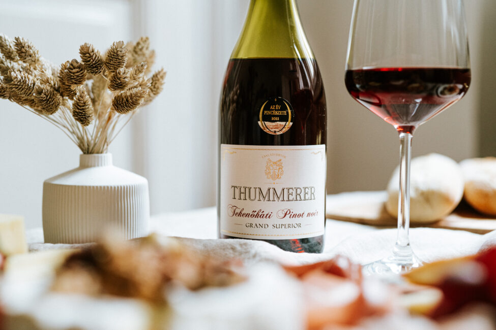 Egy palack Tekenőháti Pinot Noir Grand Superior 2016 bor egy megterített asztalon és egy kitöltött pohárral.